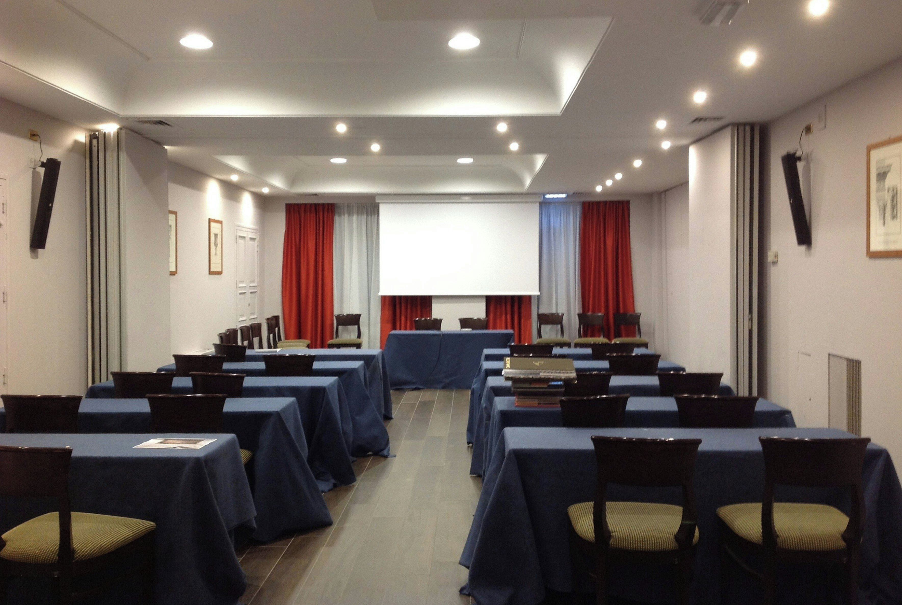 Una sala conferenze con tavoli, sedie, uno schermo per proiezioni e tende.