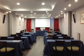 Un salón de conferencias con mesas, sillas, una pantalla de proyector y cortinas.