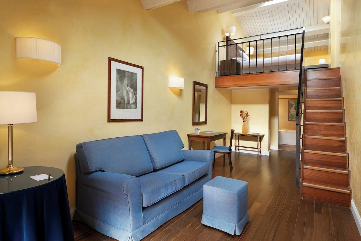 A living room with a sofa, a coffee table, a side table, a lamp, a framed picture, a small table with a vase, and a staircase leading to an upper level.