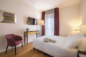 Habitación de hotel con cama, escritorio con computadora, silla, televisor y ventana con cortinas.
