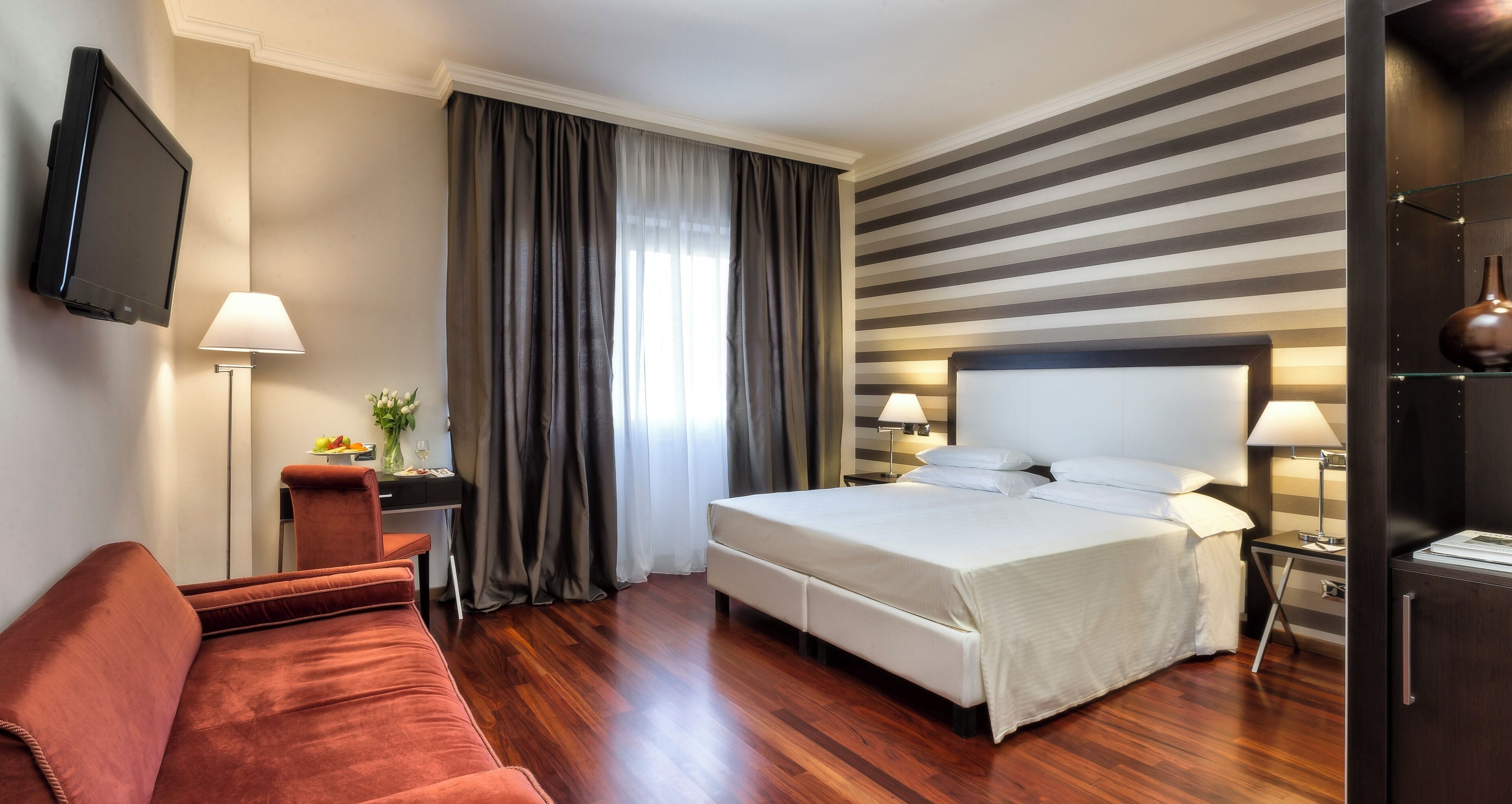 A hotel room with a bed, a sofa, a desk, a TV, and a lamp.