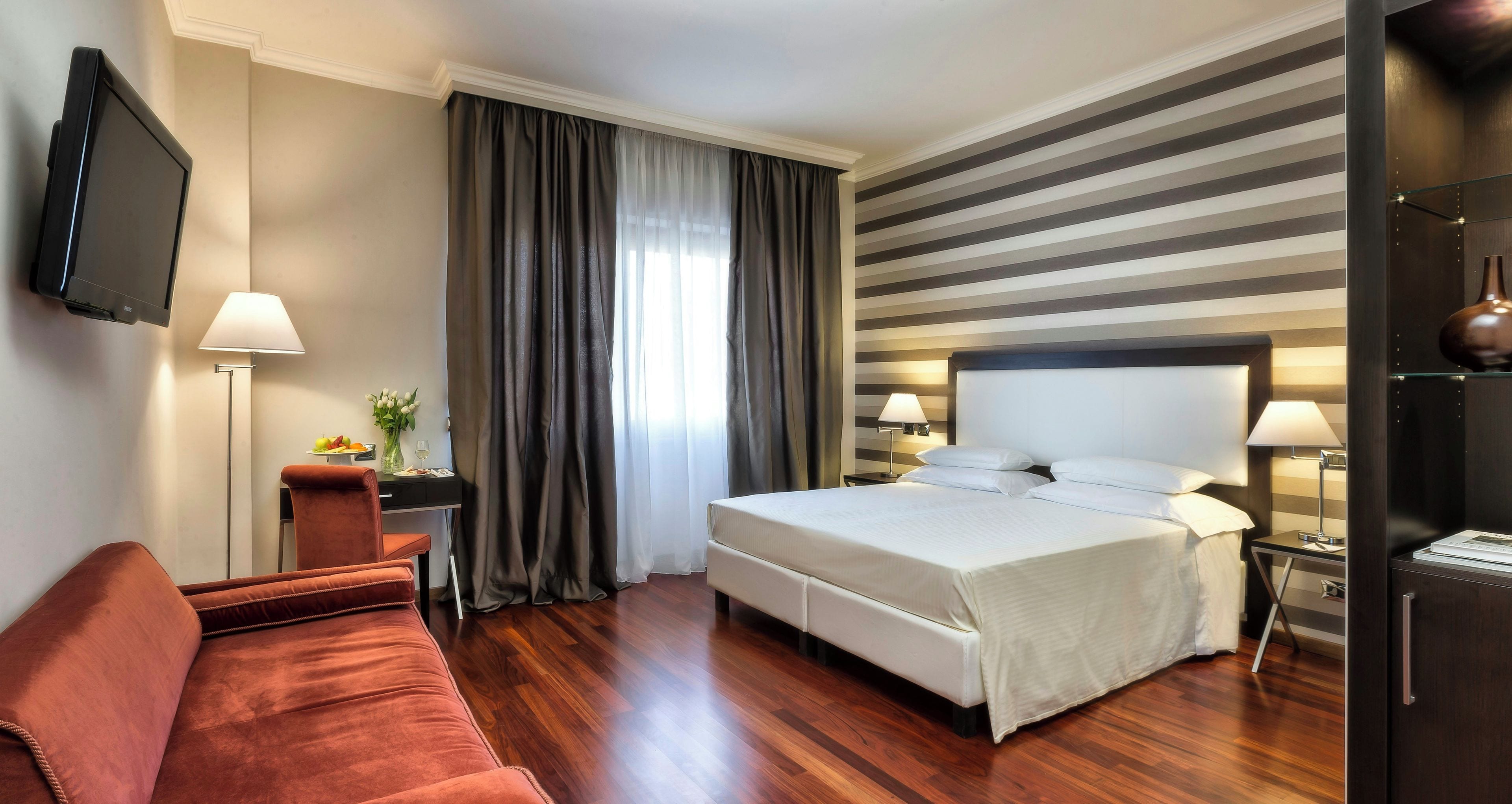 A hotel room with a bed, a desk, a TV, a sofa, and a lamp.