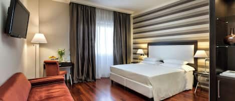 A hotel room with a bed, a desk, a TV, a sofa, and a lamp.