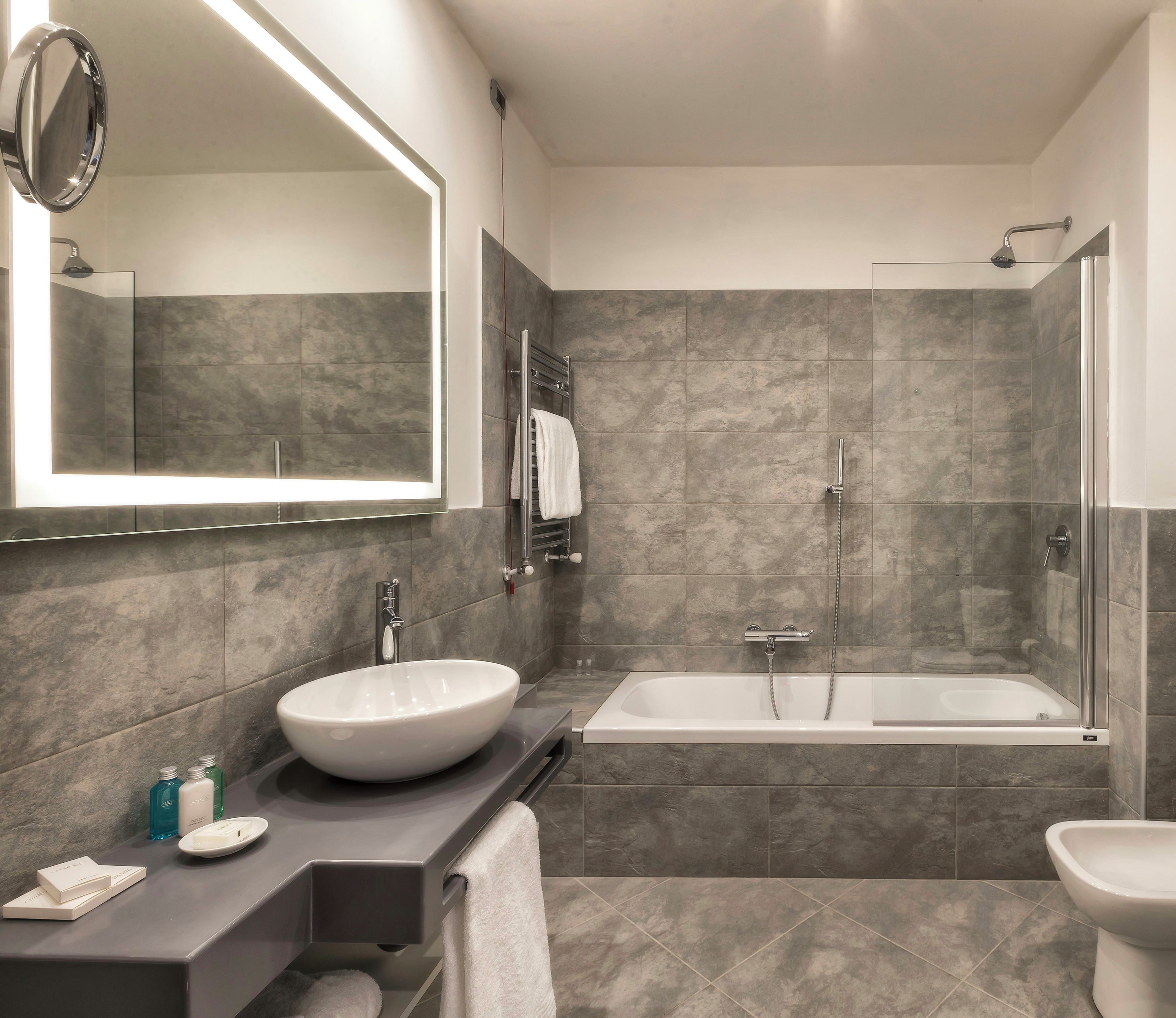 Un baño moderno con un espejo grande, un lavabo redondo, una bañera y una ducha.