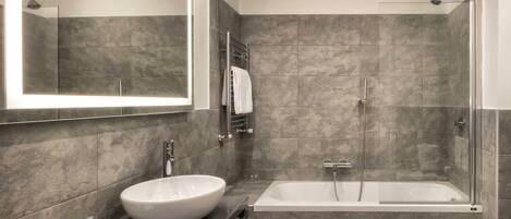 Un baño moderno con un espejo grande, un lavabo redondo, una bañera y una ducha.