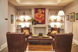 A living room with a fireplace, leather armchairs, a coffee table, and a painting above the mantel. - Sina Maria Luigia (Parma)
