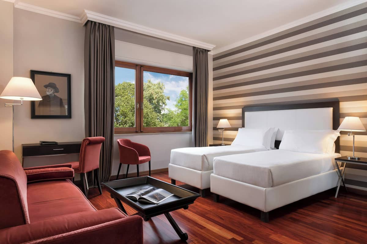 A hotel room with a bed, two bedside tables, a desk, a chair, and a sofa.