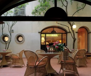 An outdoor seating area with wicker furniture, a table with a vase of flowers, and a view of the interior through an arched doorway.