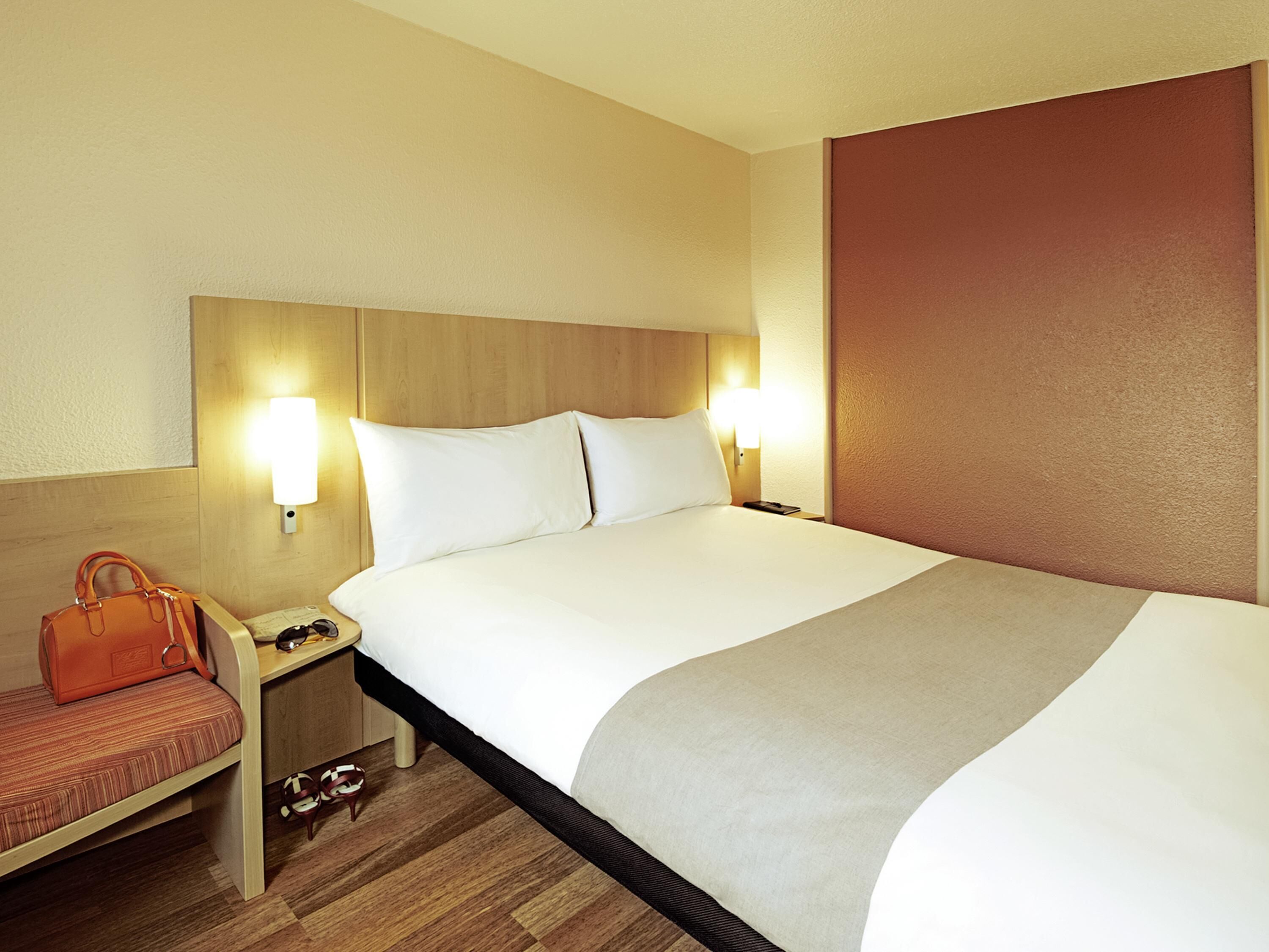 A hotel room with a large bed, two bedside lamps, a nightstand, a handbag, and a pair of shoes.