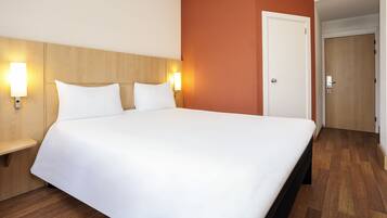 Habitación de hotel con una cama grande, cabecera de madera, dos lámparas de noche y una puerta a otra habitación.