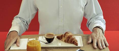A person seated at a table with a croissant, a cup of coffee, and a glass of orange juice.