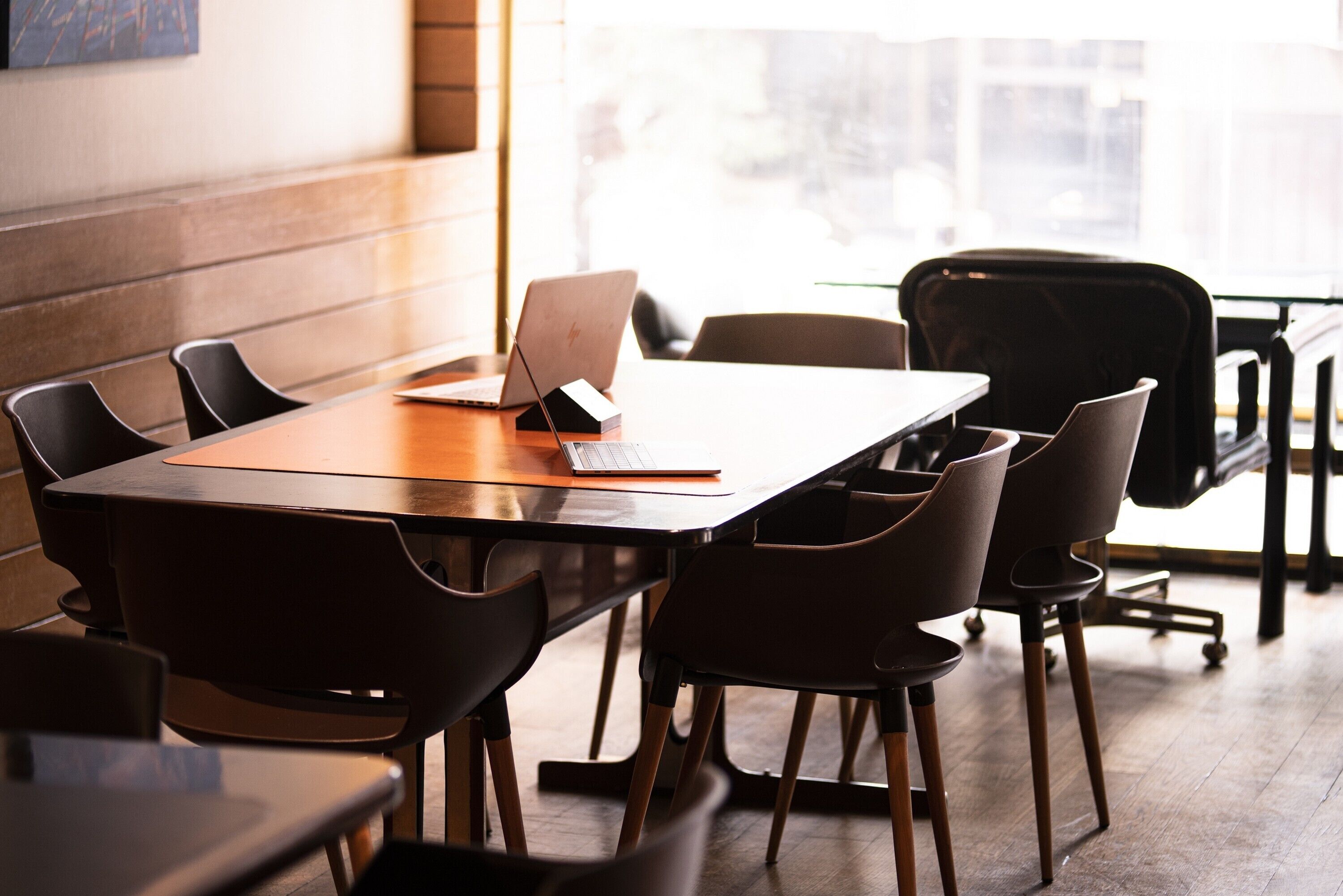 Uma sala de conferência com uma mesa de madeira, cadeiras pretas e um laptop.