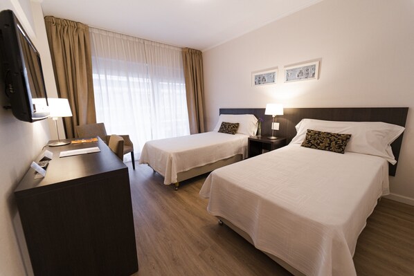 A hotel room with two beds, a desk with a lamp, a TV, and a window with curtains. - El Conquistador Hotel (Buenos Aires)