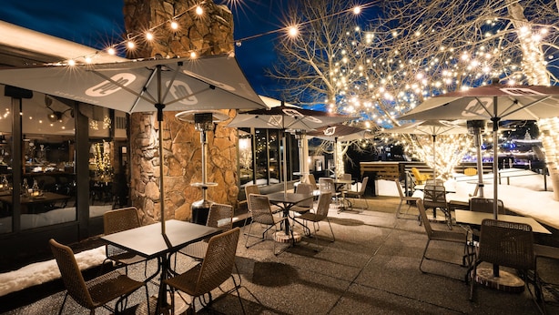 Un espace extérieur aménagé en terrasse, avec des tables et des chaises, des murs en pierre et des guirlandes lumineuses.
