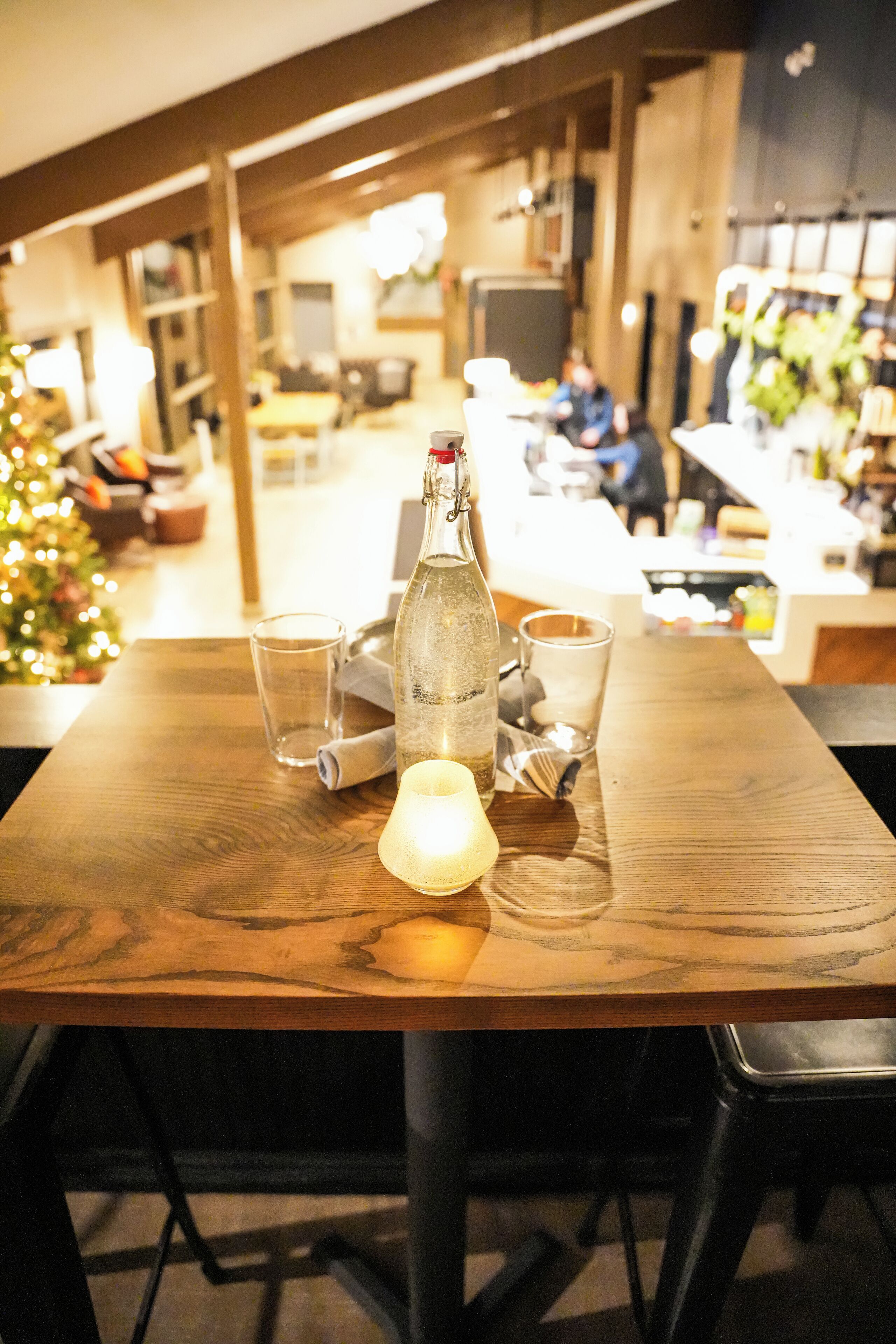 Una mesa de madera con una botella, vasos y una vela.