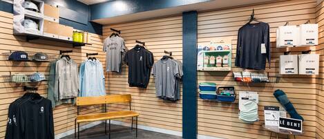 A retail store with clothing racks, a wooden bench, and shelves with boxes and products.