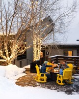 Un grupo de personas sentadas en una mesa de madera al aire libre, rodeadas de nieve y árboles decorados.