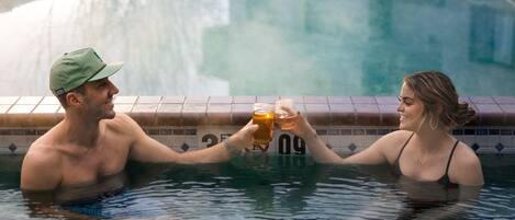 A couple in a swimming pool holding drinks.
