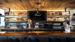 Un bar avec un plafond en bois, des étagères remplies de bouteilles d’alcool, des verres et un comptoir avec des tabourets.