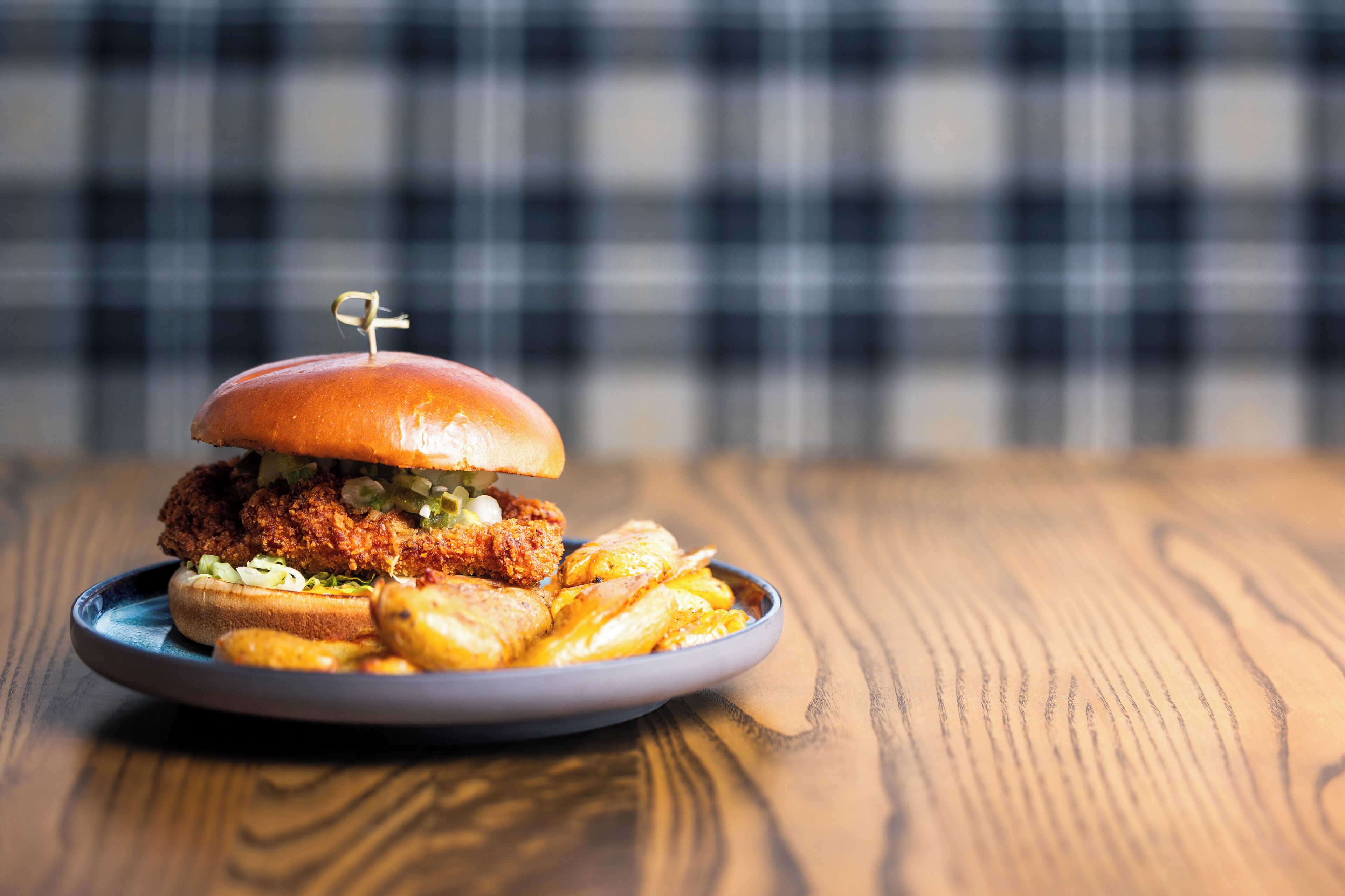 Un plato con un sándwich de pollo frito y papas fritas sobre una mesa de madera.
