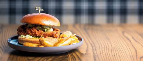 Un plato con un sándwich de pollo frito y papas fritas sobre una mesa de madera.