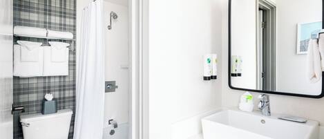 Baño con inodoro, ducha y lavamanos. Se observan toallas y artículos de aseo.