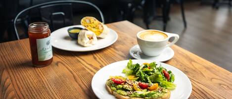 Een houten tafel met avocado-toast, een kop koffie en een pot jam.