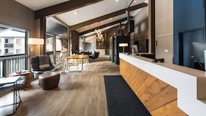 Un intérieur moderne avec un comptoir d’accueil en bois, un espace repas comprenant une table et des chaises, et une grande fenêtre donnant sur l’extérieur.