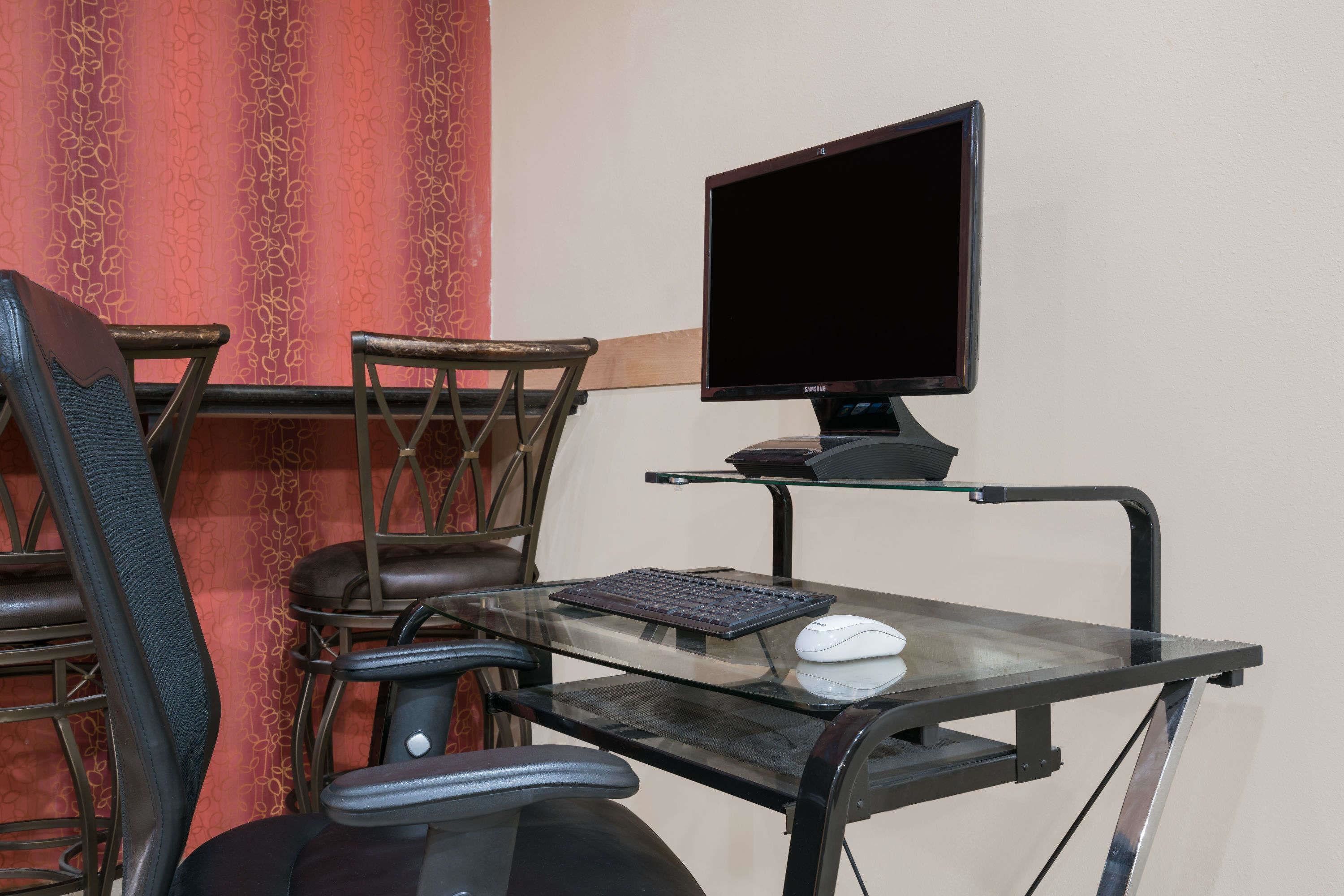 A modern office setup with a glass desk, black and brown office chairs, a computer monitor, keyboard, and mouse.