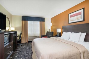 A hotel room with a bed, a desk with a computer, a chair, and a television.