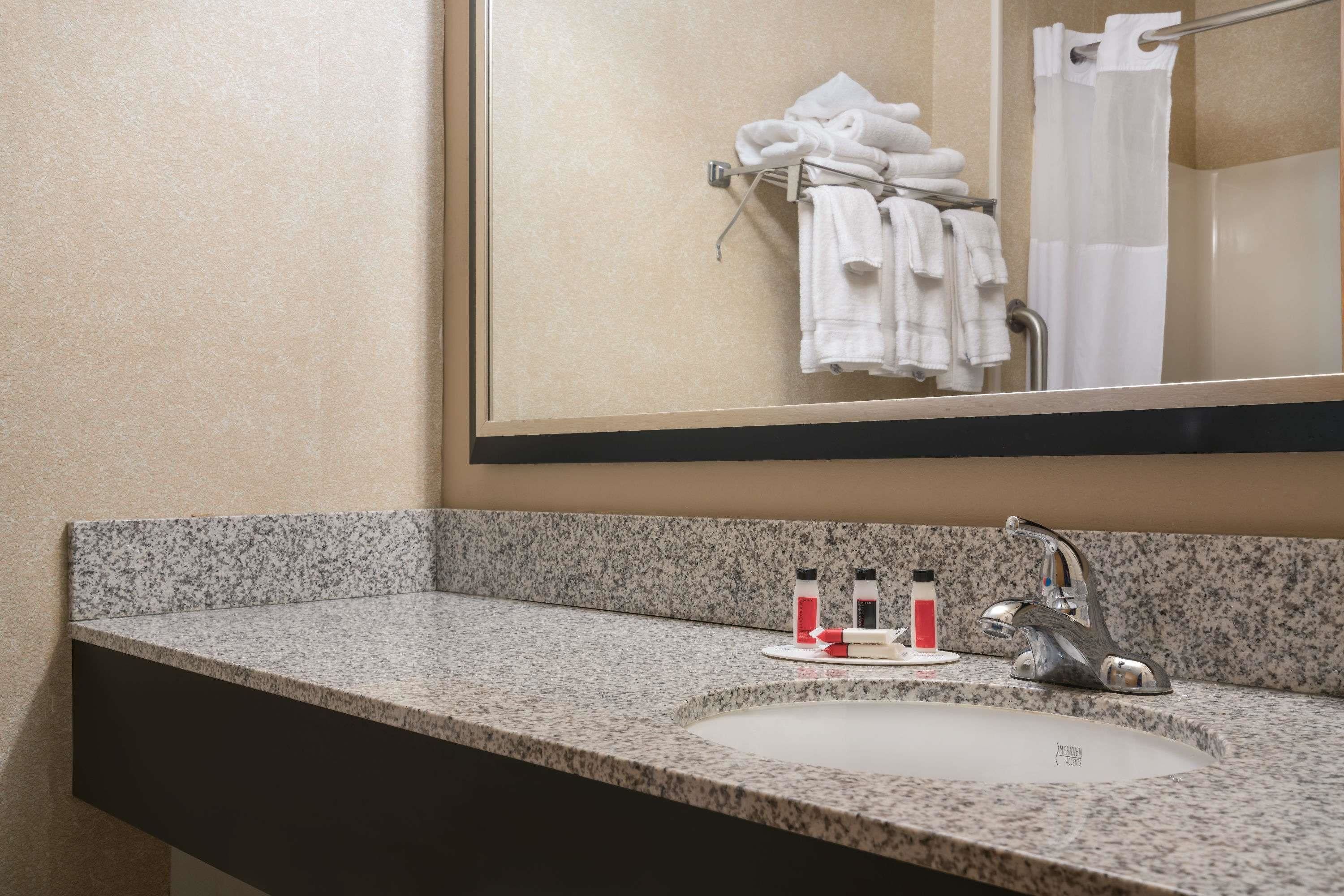 A bathroom with a granite countertop, a sink, a mirror, and a towel rack with folded towels.