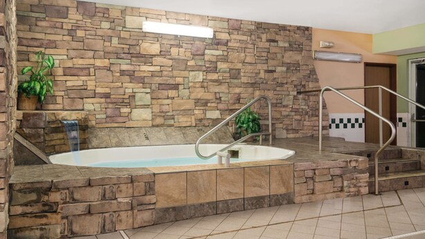 A stone-walled indoor pool area with a built-in hot tub, a metal handrail, and a potted plant. - Quality Inn & Suites Mankato East (Mankato)