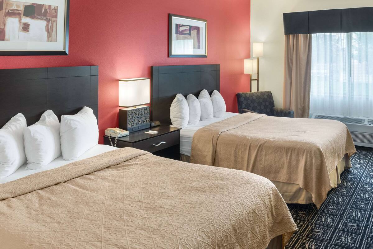 A hotel room with two beds, a nightstand, a chair, and a large window with curtains.