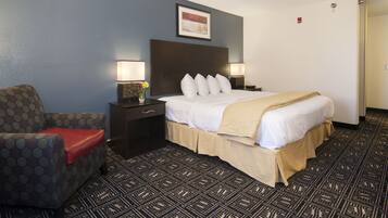 A hotel room with a bed, a nightstand, a lamp, a chair, and a patterned carpet.