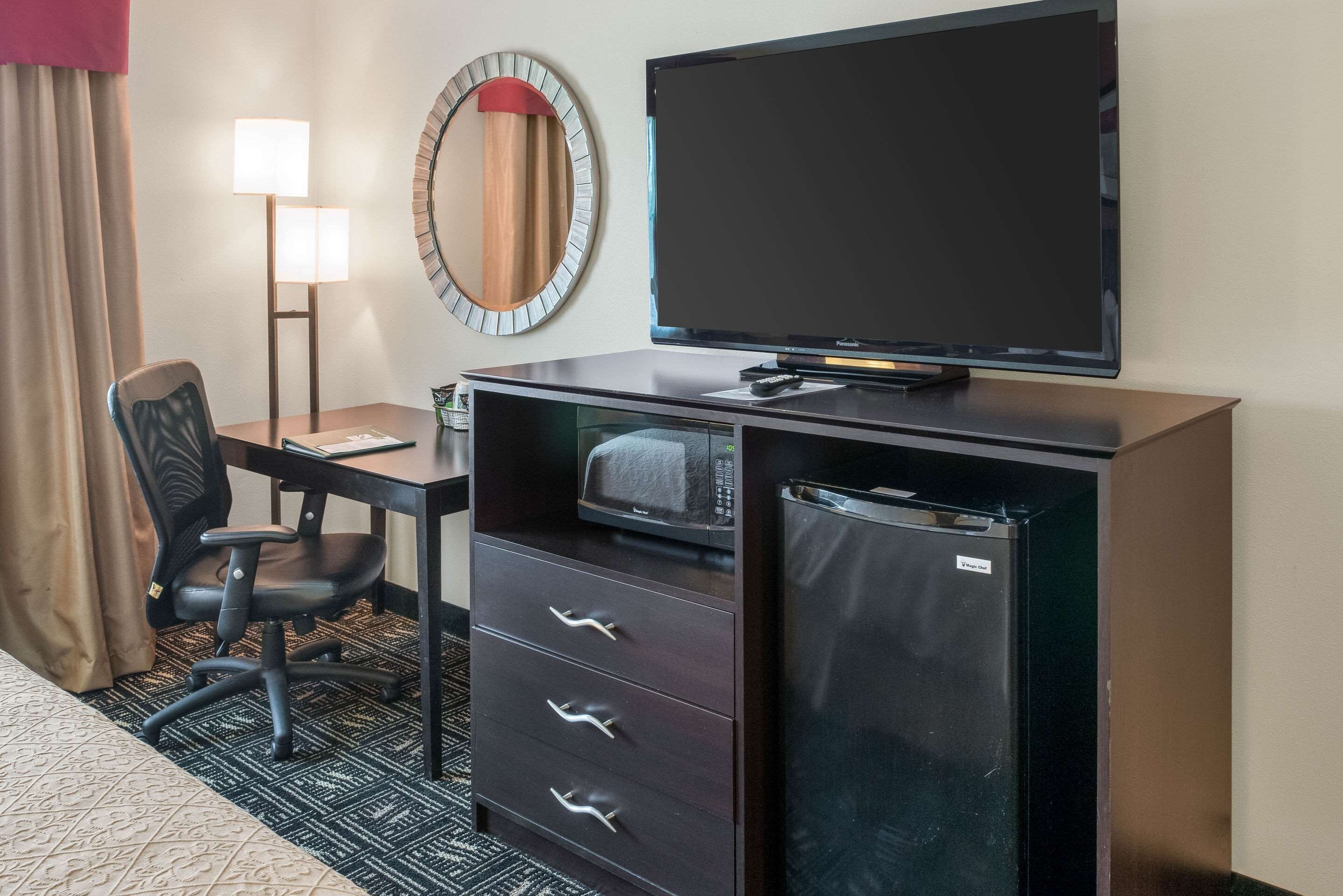 Habitación de hotel con escritorio, silla, televisor de pantalla plana, microondas y refrigerador.