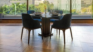 A dining area with a table set for four, two chairs, and a view of a cityscape with modern buildings and a dome structure. - Fiesta Americana Reforma (Mexico City)