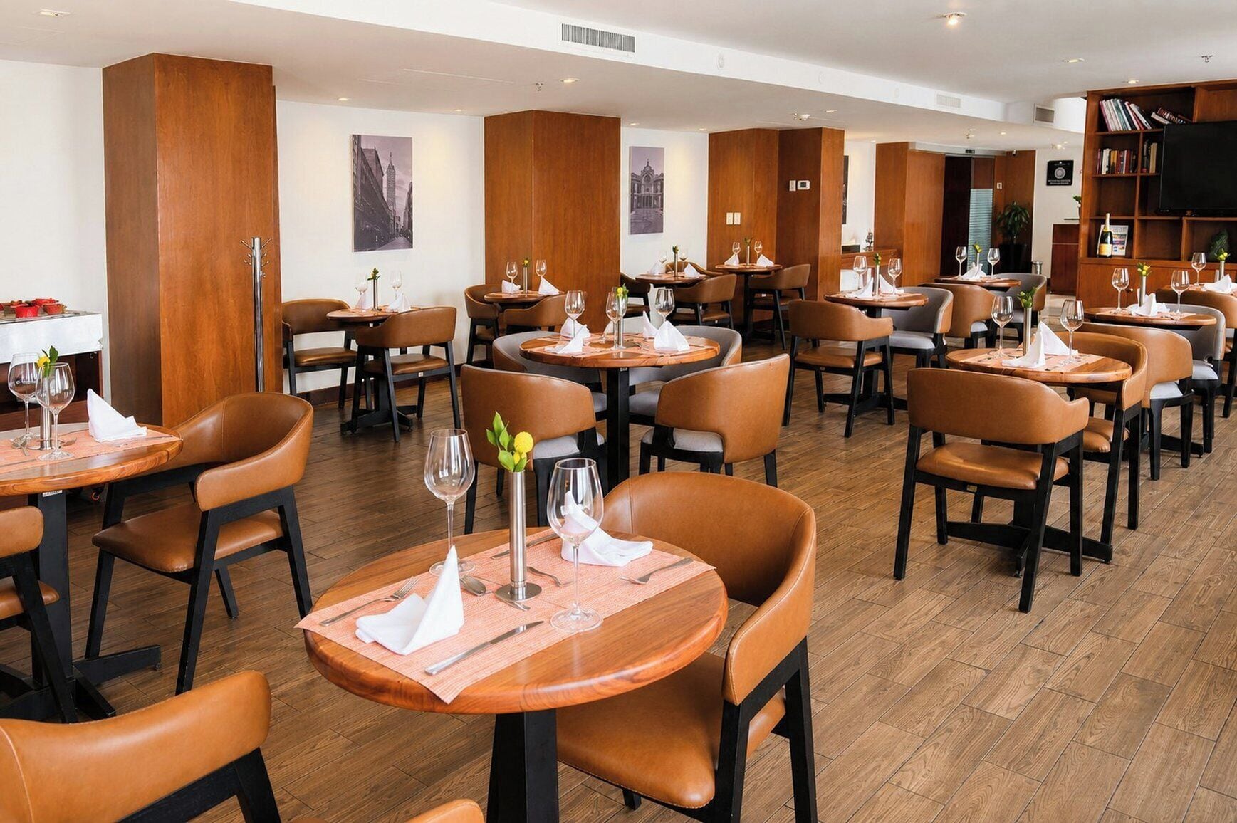 A restaurant with round tables, brown leather chairs, and wooden paneling.