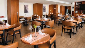 Un restaurante con mesas redondas, sillas de cuero marrón y paneles de madera.