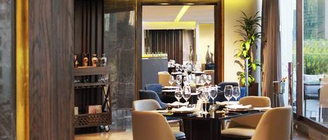 A modern dining area with a long table, chairs, and wine glasses.