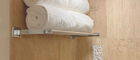 A bathroom with a wooden wall, a towel rack holding two rolled towels, and a decorative panel with a leaf pattern.
