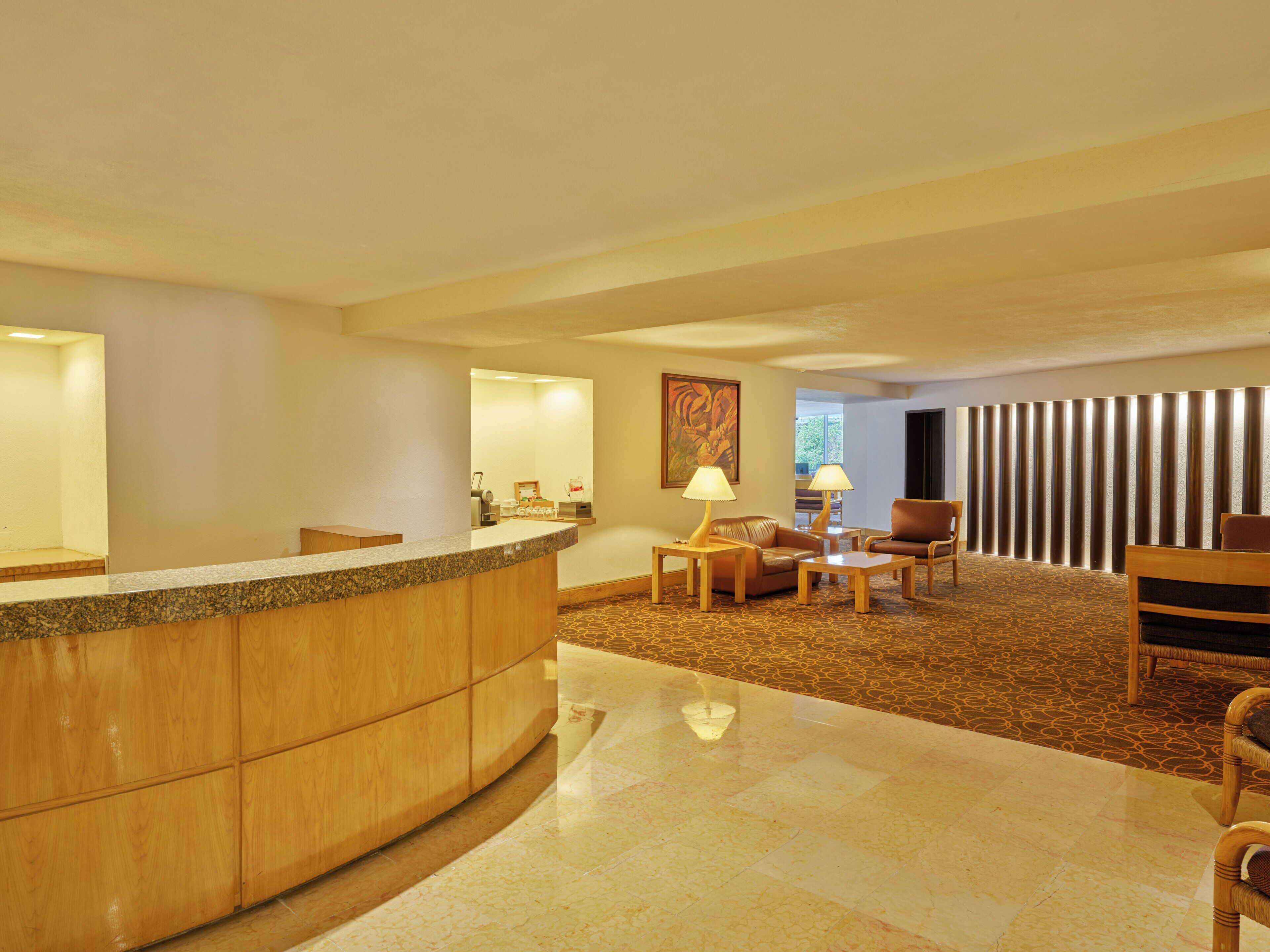 Un vestíbulo de hotel con mostrador de recepción, zona de estar y un espejo grande.