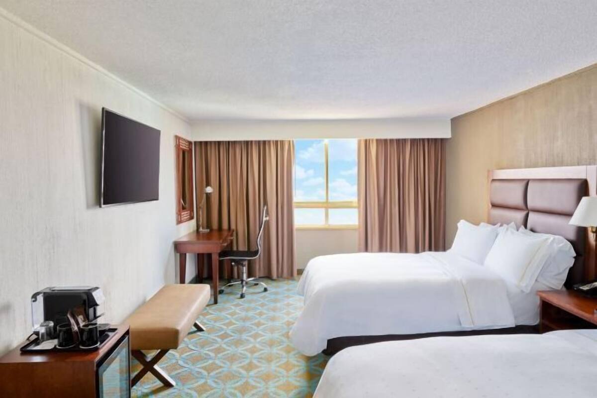 A hotel room with two beds, a desk, a chair, a TV, and a window with curtains.
