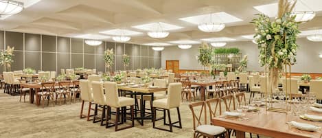 A large banquet hall with multiple round tables, chairs, and a high ceiling with skylights.
