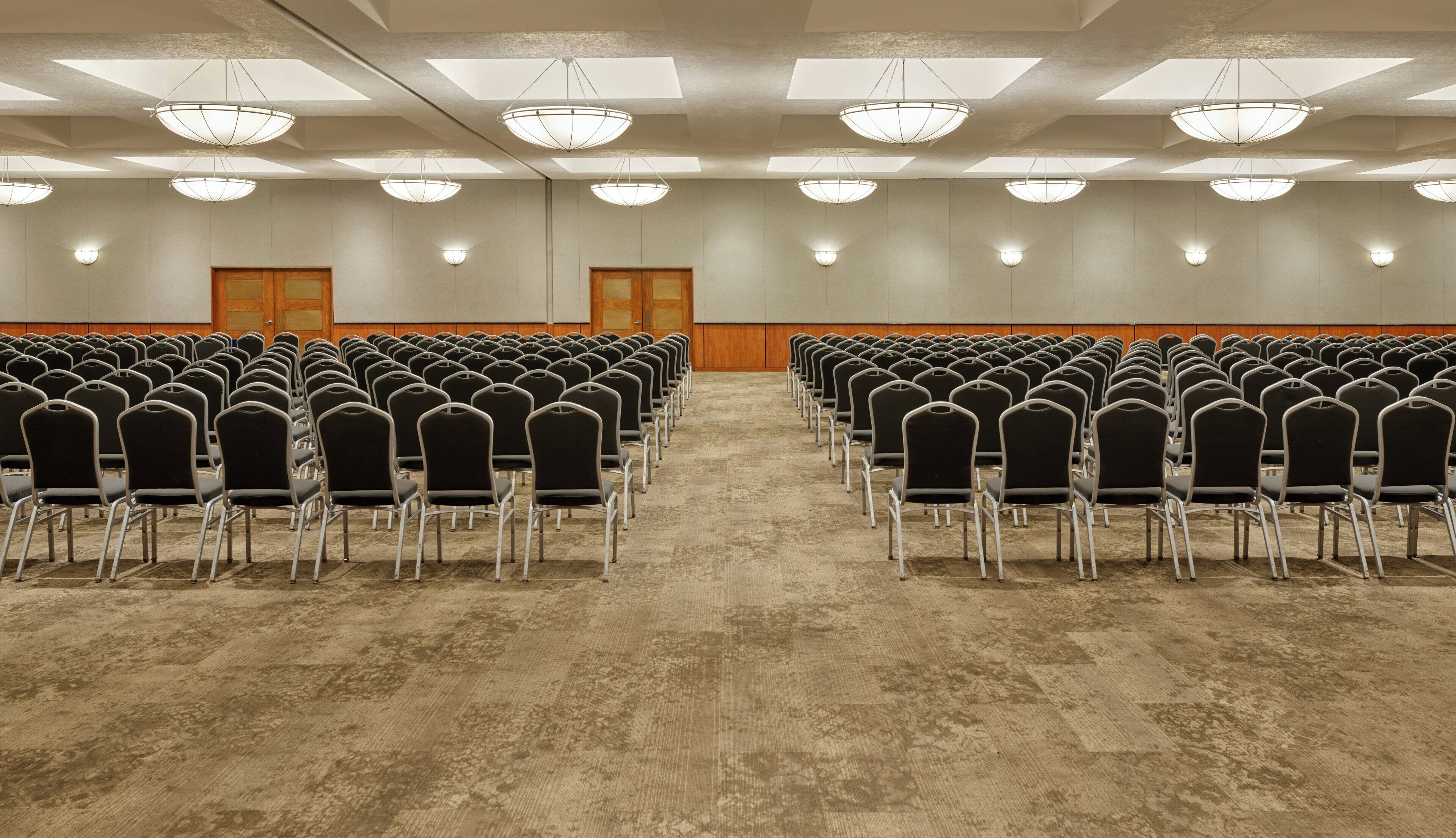 Un salón de conferencias con filas de sillas, luces en el techo y suelo alfombrado.