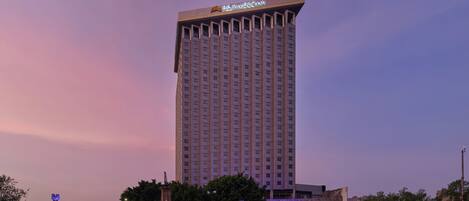 Un hotel alto con un letrero llamativo en la parte superior, rodeado de árboles y una calle bien iluminada.
