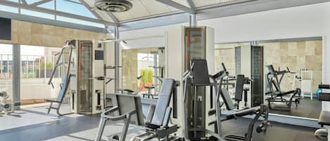 Een sportschool met diverse fitnessapparaten, een grote spiegel en uitzicht naar buiten.