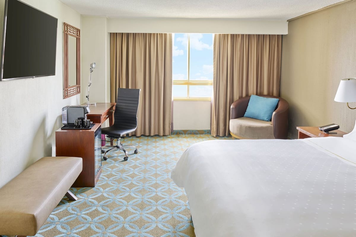 A hotel room with a bed, a desk with a chair, a sofa, a TV, and a window with curtains.