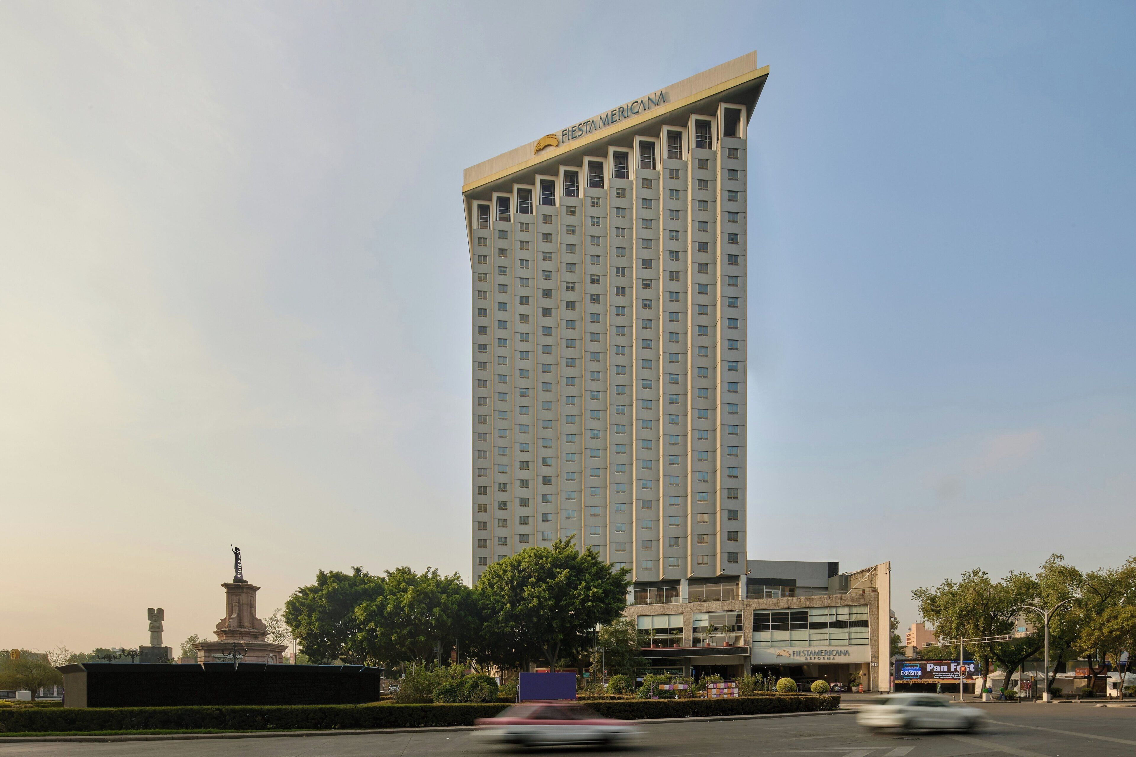 A tall hotel with a modern design, a statue in front, and a Panera Bread sign nearby.