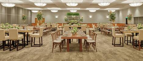 Un gran salón de banquetes con múltiples mesas redondas, cada una dispuesta con sillas, centros de mesa y una araña colgante.