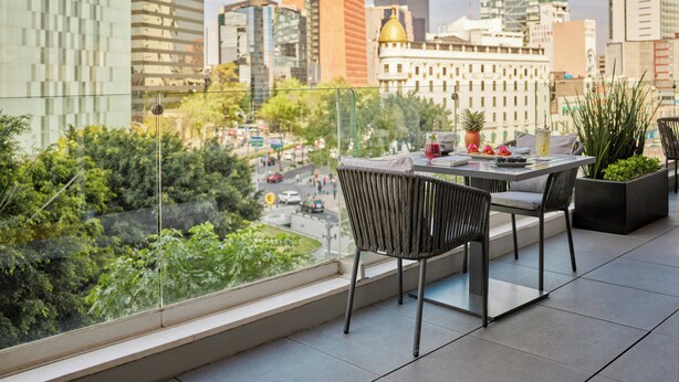 A balcony with a table and chairs, a potted plant, and a view of a cityscape with buildings and greenery. - Fiesta Americana Reforma (Mexico City)